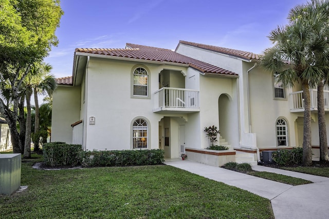 mediterranean / spanish home featuring a tile roof, a balcony, a front lawn, and stucco siding