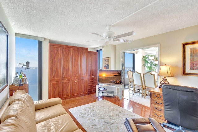 home office featuring ceiling fan, a water view, light wood-type flooring, and a textured ceiling