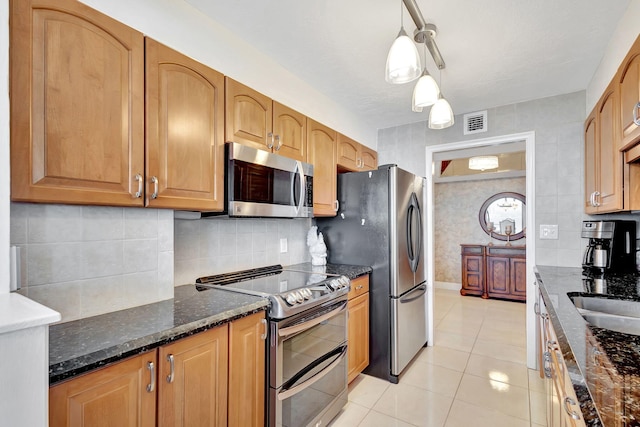 kitchen with hanging light fixtures, dark stone counters, decorative backsplash, light tile patterned flooring, and appliances with stainless steel finishes