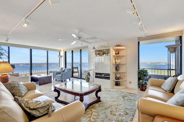 tiled living room with ceiling fan, a water view, and a wall of windows