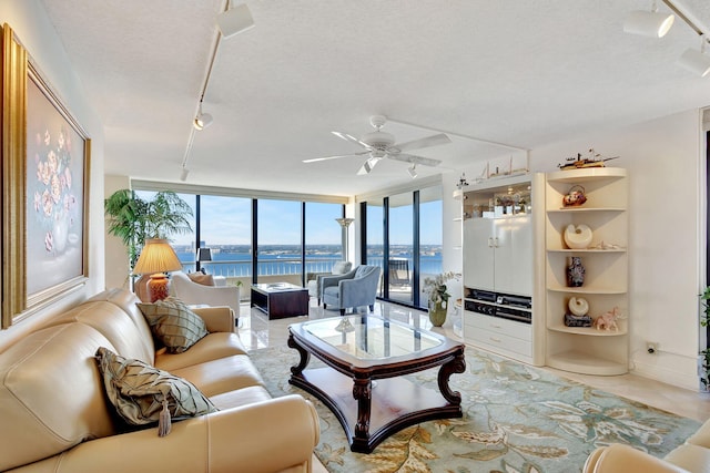 living room featuring expansive windows, ceiling fan, a water view, and a textured ceiling