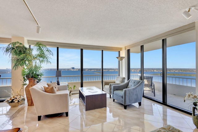 living room featuring expansive windows, plenty of natural light, a textured ceiling, a water view, and light tile patterned floors