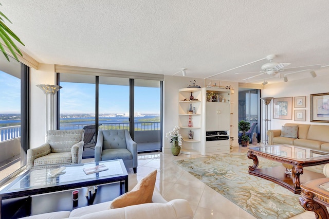 living room featuring a wealth of natural light, a textured ceiling, ceiling fan, light tile patterned floors, and a water view