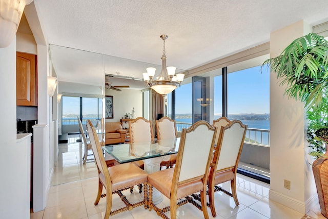 dining area featuring ceiling fan with notable chandelier, light tile patterned flooring, a water view, and a textured ceiling