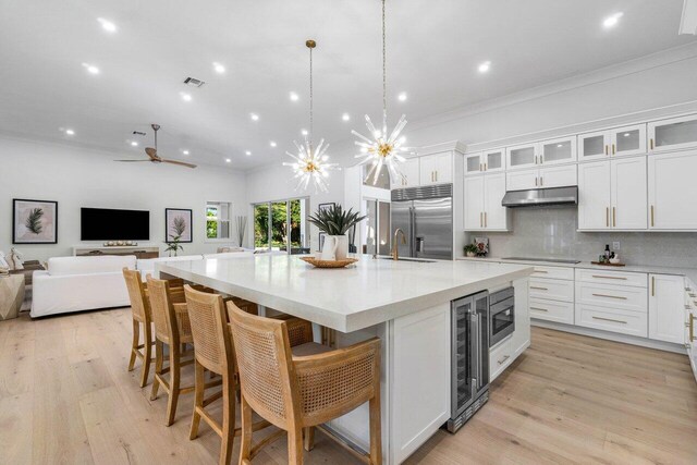 kitchen featuring hanging light fixtures, built in appliances, wine cooler, white cabinets, and a large island with sink