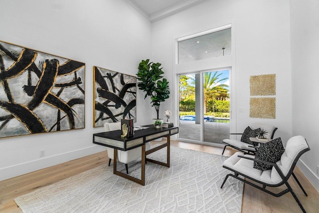 office area with ornamental molding, a towering ceiling, and light hardwood / wood-style floors