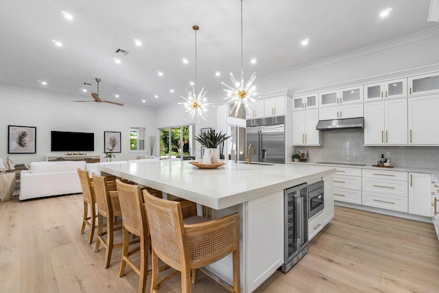 kitchen featuring wine cooler, built in appliances, hanging light fixtures, a large island, and white cabinets