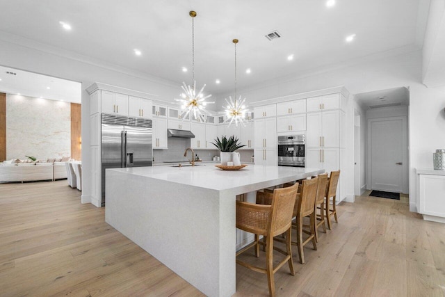 kitchen with crown molding, white cabinetry, hanging light fixtures, stainless steel appliances, and a spacious island