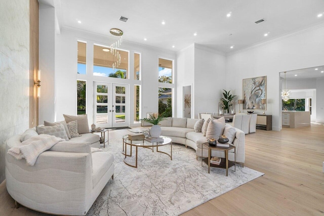 living room with crown molding, a towering ceiling, light wood-type flooring, and french doors