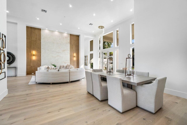 dining area featuring ornamental molding, a towering ceiling, and light wood-type flooring