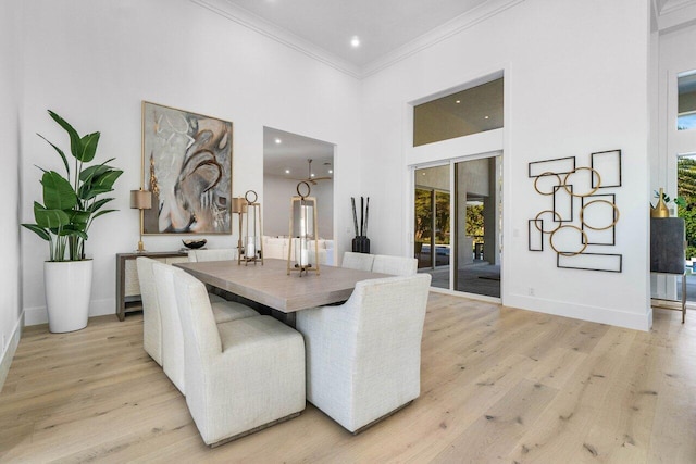 dining area with light hardwood / wood-style flooring, ornamental molding, and a high ceiling