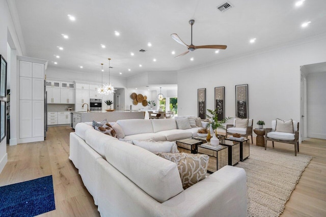 living room with ceiling fan with notable chandelier, ornamental molding, sink, and light wood-type flooring