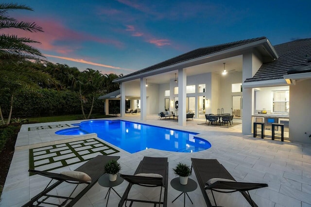 pool at dusk featuring a patio area, an outdoor bar, and ceiling fan