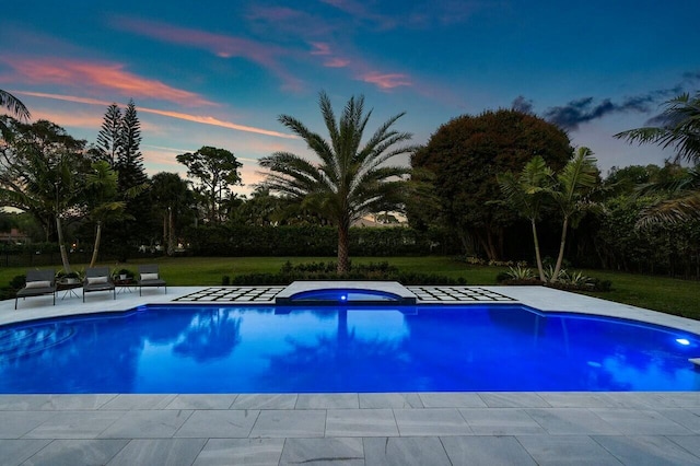 pool at dusk with a patio area and a lawn