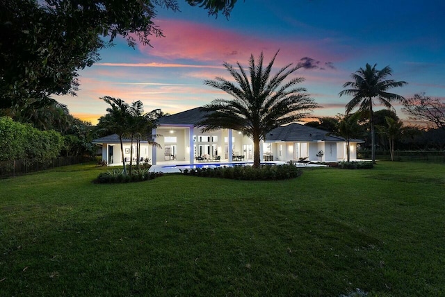 back house at dusk with a pool and a lawn