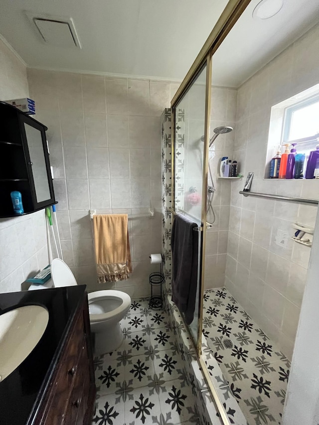 bathroom with toilet, tile walls, a shower with door, tile patterned floors, and vanity