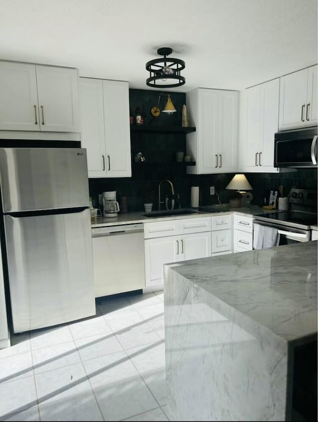 kitchen with light stone counters, white cabinetry, stainless steel appliances, and a sink