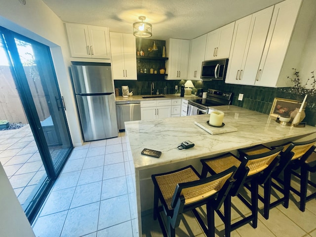 kitchen featuring appliances with stainless steel finishes, a peninsula, a sink, backsplash, and light tile patterned flooring