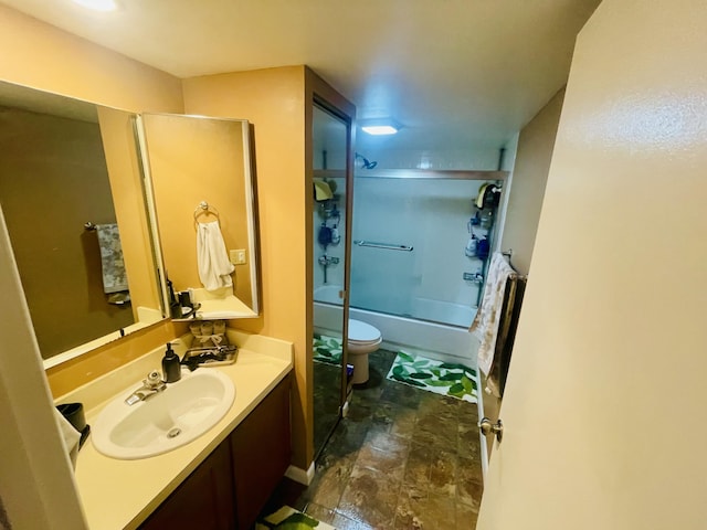 full bathroom featuring toilet, stone finish flooring, bath / shower combo with glass door, and vanity