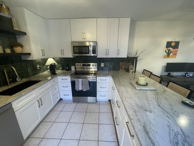 kitchen featuring light tile patterned floors, stainless steel appliances, open shelves, a sink, and light stone countertops