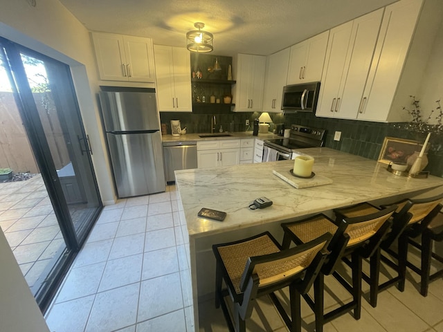 kitchen with stainless steel appliances, a peninsula, a sink, and white cabinetry