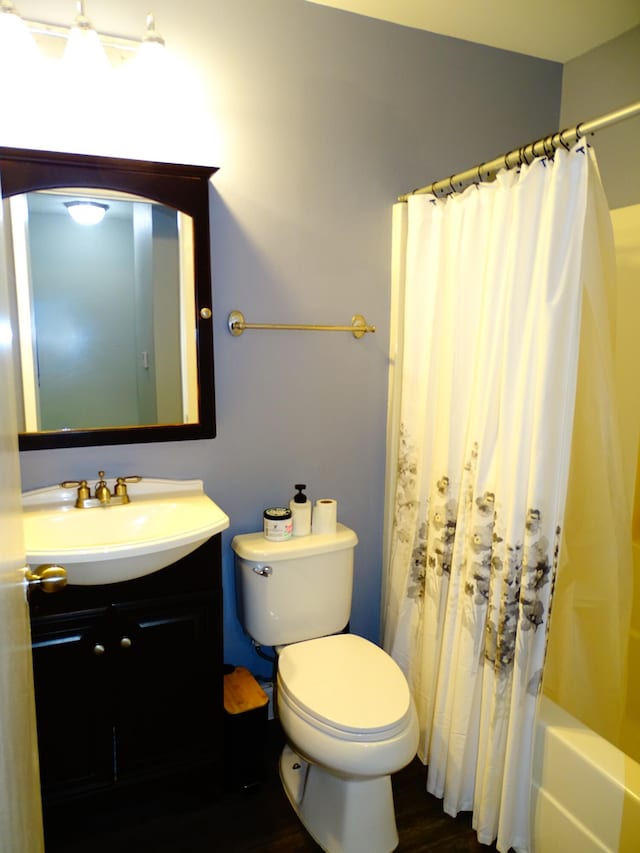 full bathroom featuring hardwood / wood-style flooring, shower / tub combo with curtain, vanity, and toilet