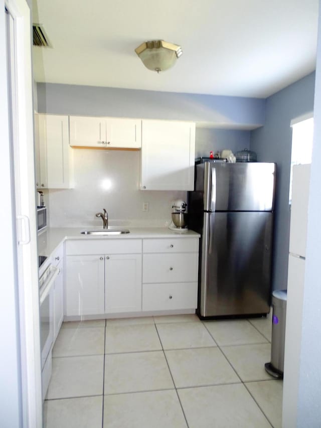 kitchen featuring white cabinets, sink, light tile patterned floors, range, and stainless steel refrigerator