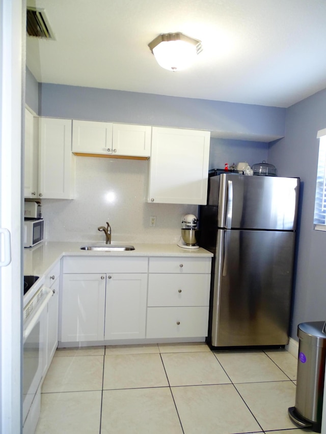 kitchen featuring stainless steel fridge, stove, white cabinetry, and sink