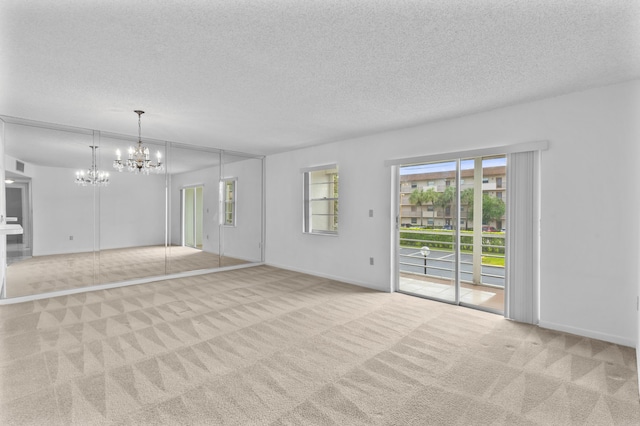 unfurnished living room with a textured ceiling, a notable chandelier, and light carpet