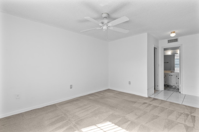 unfurnished room with ceiling fan, a textured ceiling, and light carpet