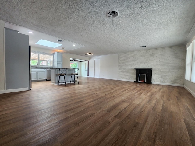 unfurnished living room featuring sink, a skylight, a textured ceiling, dark hardwood / wood-style flooring, and brick wall