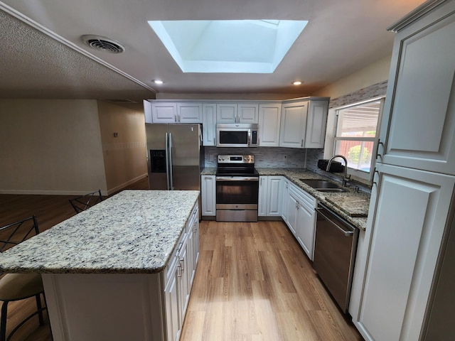 kitchen featuring a center island, sink, a skylight, appliances with stainless steel finishes, and tasteful backsplash