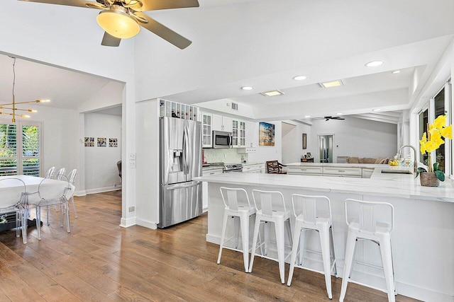 kitchen featuring kitchen peninsula, stainless steel appliances, sink, white cabinetry, and a breakfast bar area