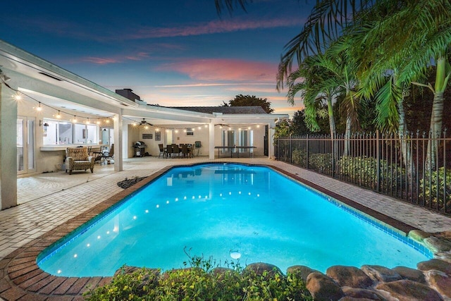 pool at dusk with ceiling fan and a patio