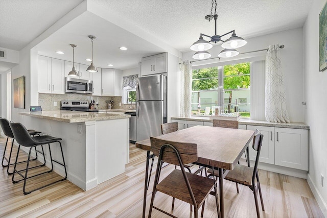 kitchen with pendant lighting, backsplash, white cabinets, kitchen peninsula, and stainless steel appliances