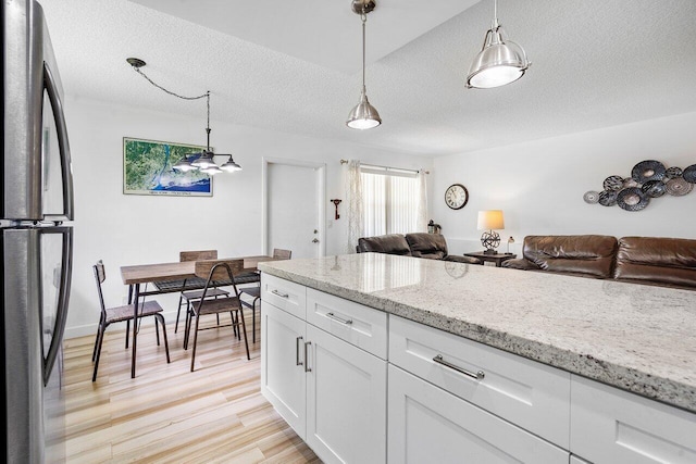 kitchen with stainless steel refrigerator, light stone countertops, white cabinets, and hanging light fixtures