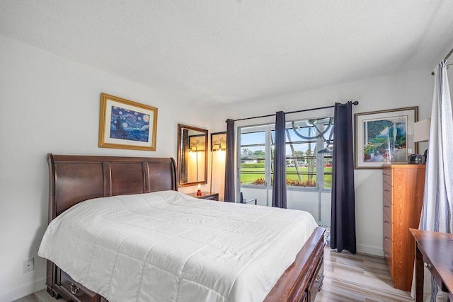 bedroom featuring access to outside, light hardwood / wood-style floors, and a textured ceiling