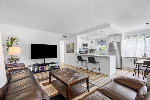 living room featuring sink, a textured ceiling, and light wood-type flooring