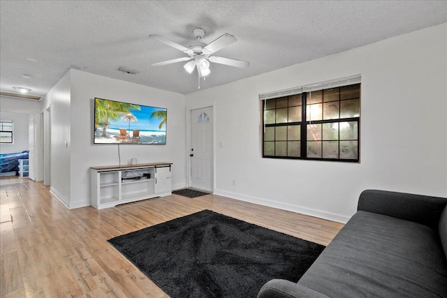 living room featuring ceiling fan, light wood-type flooring, and a textured ceiling