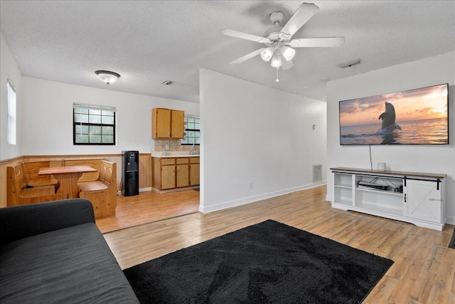 living room featuring ceiling fan, light wood-type flooring, and a textured ceiling