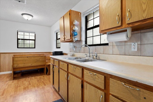 kitchen with a textured ceiling, decorative backsplash, sink, and light hardwood / wood-style flooring