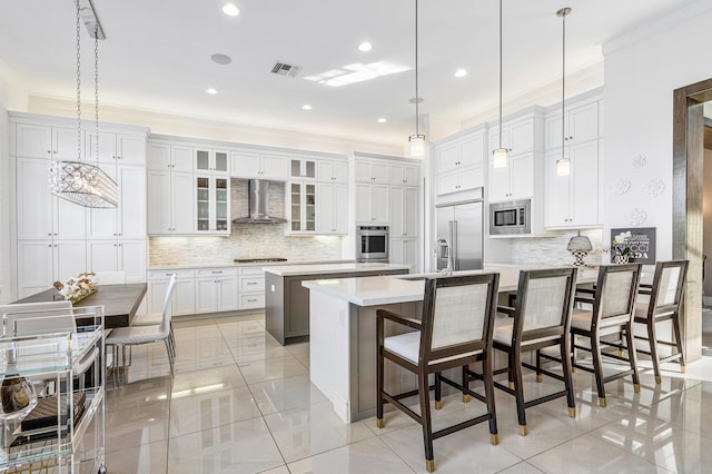 kitchen featuring built in appliances, a breakfast bar, wall chimney range hood, and an island with sink