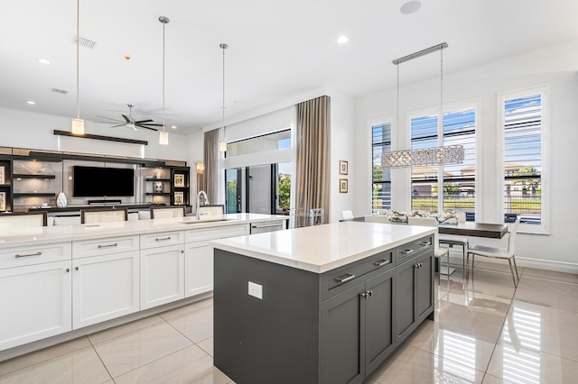 kitchen with a kitchen island with sink, sink, light tile patterned floors, decorative light fixtures, and white cabinets