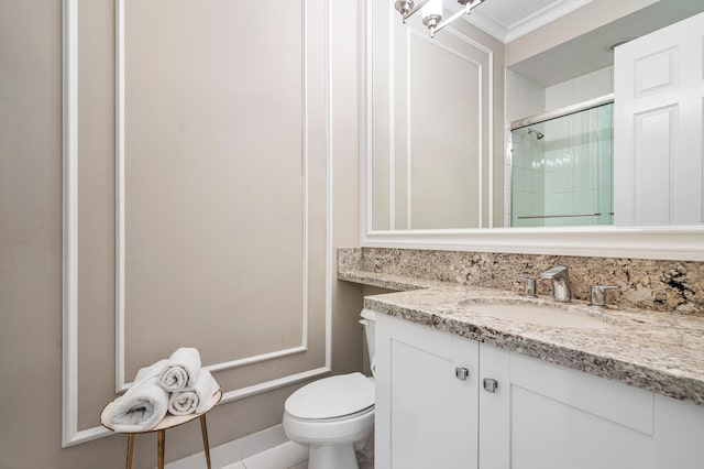 bathroom with toilet, vanity, an enclosed shower, and ornamental molding