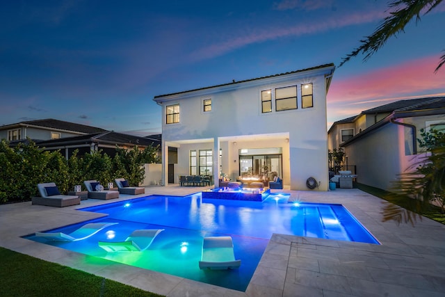 back house at dusk featuring a patio and a pool with hot tub