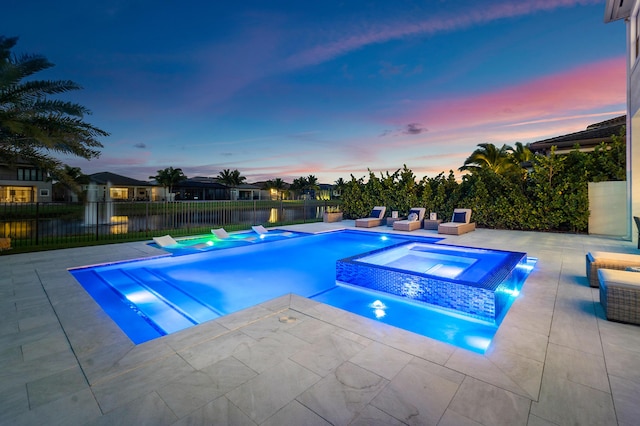 pool at dusk with an in ground hot tub and a patio area