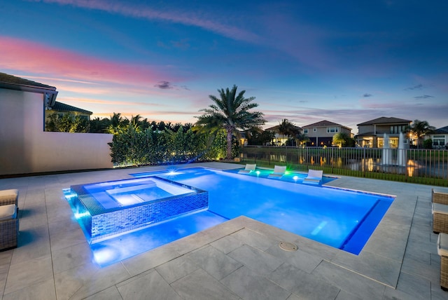 pool at dusk featuring an in ground hot tub and a patio