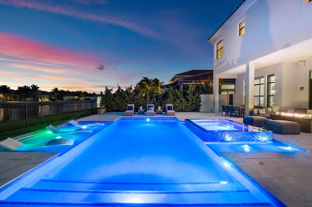 pool at dusk featuring an in ground hot tub, an outdoor living space, and a patio