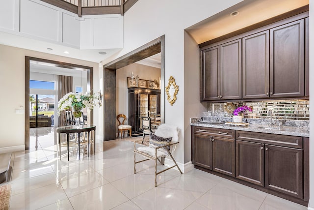 bar featuring dark brown cabinets, backsplash, light stone counters, and sink