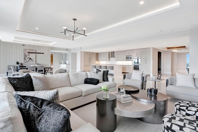 living room featuring sink, a tray ceiling, and a notable chandelier